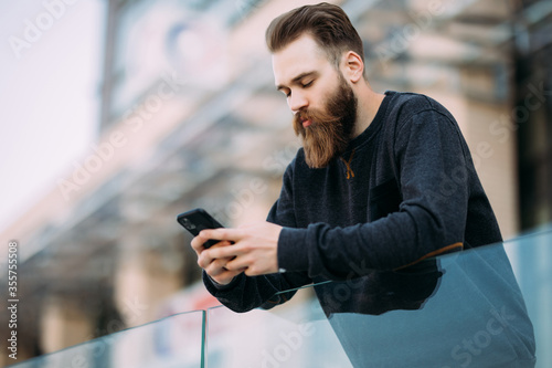 Portrait of bearded male typing in mobile while outdoor in the street