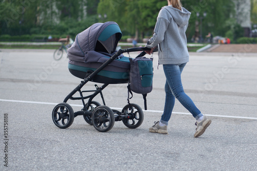A girl, a young mother with a stroller is walking along a city street.
