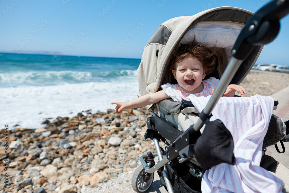 a little girl in a stroller points to the sea
