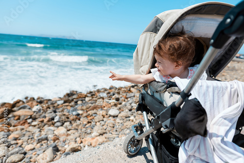 a child in a stroller points to the sea