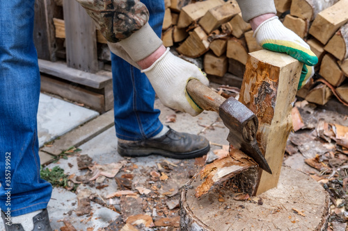 A man cleans the bark from birch wood with a metal ax with a wooden handle. Logging firewood for the fireplace insert.