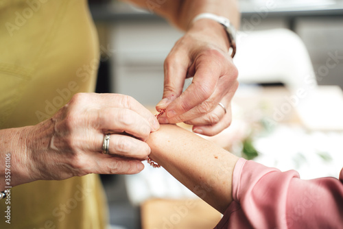 Elderly woman helping young woman to dress. Close up of hands fastening bracelet on wrist.