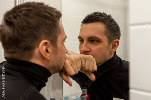 Portrait of a young short haired man wearing black turtleneck and looking in the mirror. reflection of a young guy looking in a mirror.