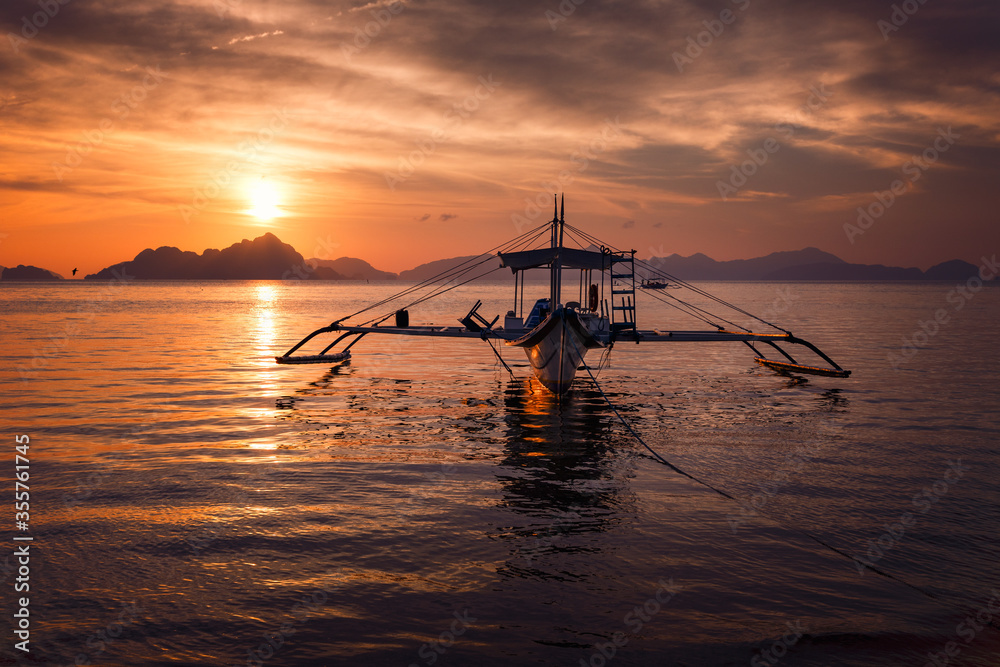 Traditional boat on the background of a bright sunset and a series of tropical Islands.