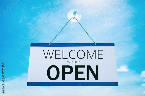 COVID-19 WELCOME we are Open for business hanging on store front window sign for stores reopening after coronavirus. Cafe, businesses, restaurants, reopen again. Sunny summer blue sky window