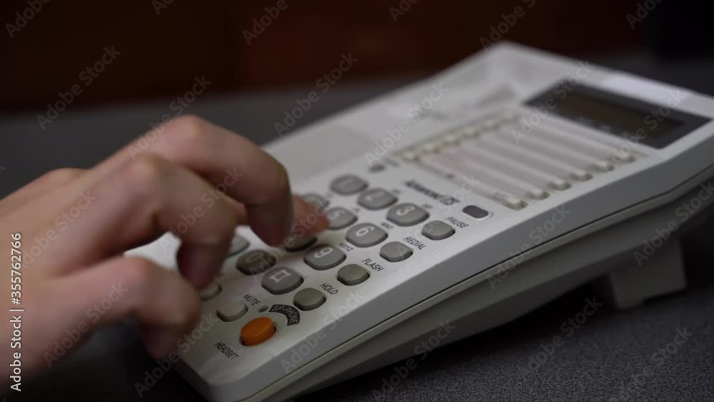 Men Hand Dials On The Number Buttons On The A Wired Phone. Low angle closeup view of male hand picking up handset and dialing telephone number on white landline phone keypad. Men Hand Dials On The Number Buttons On The A Wired Phone. Low angle closeup view of male hand picking up handset and dialing telephone number on white landline phone keypad.