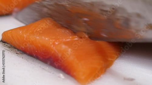 Close-up of cutting fresh salmon fillet using a white chopping board. Preparing raw fish steak in the kitchen.