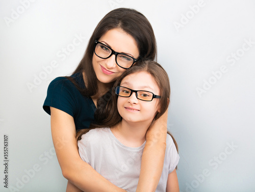 Happy young casual mother and smiling kid in fashion glasses hugging on light blue background with empty copy space. Closeup natural family portrait
