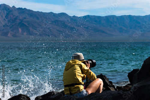 Photographer woman captured while shooting wildlife on a beautiful seascape with mountain range and turquoise water in Baja California © Aleksandra