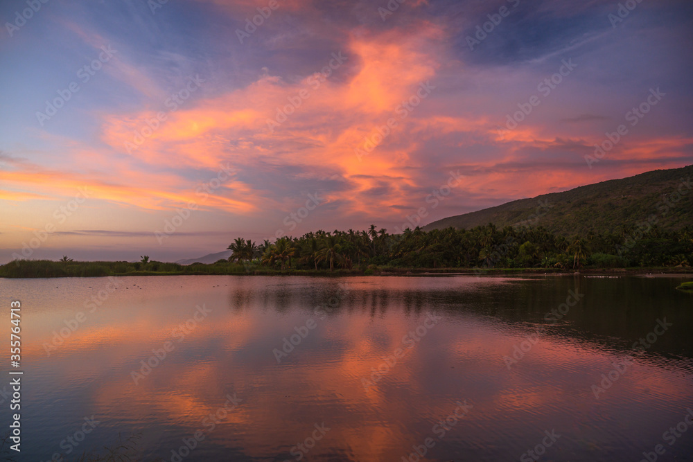 Exotic sunset landscape with vibrant pink clouds green palms and mountain hills in the background in Mexico