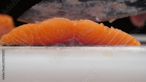 Side view of slicing raw salmon fish fillet on a white chopping board. Cutting fresh fish steak at home.