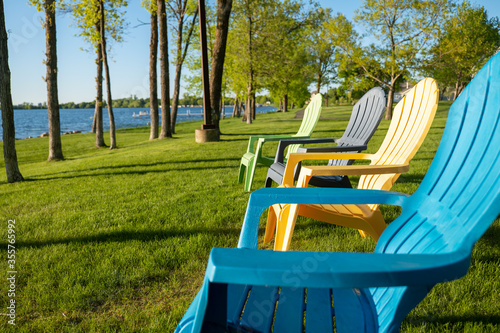 Εκτύπωση καμβά Colorful adirondack chairs on the green grass near the shoreline of a beautiful Minnesota lake on a sunny evening