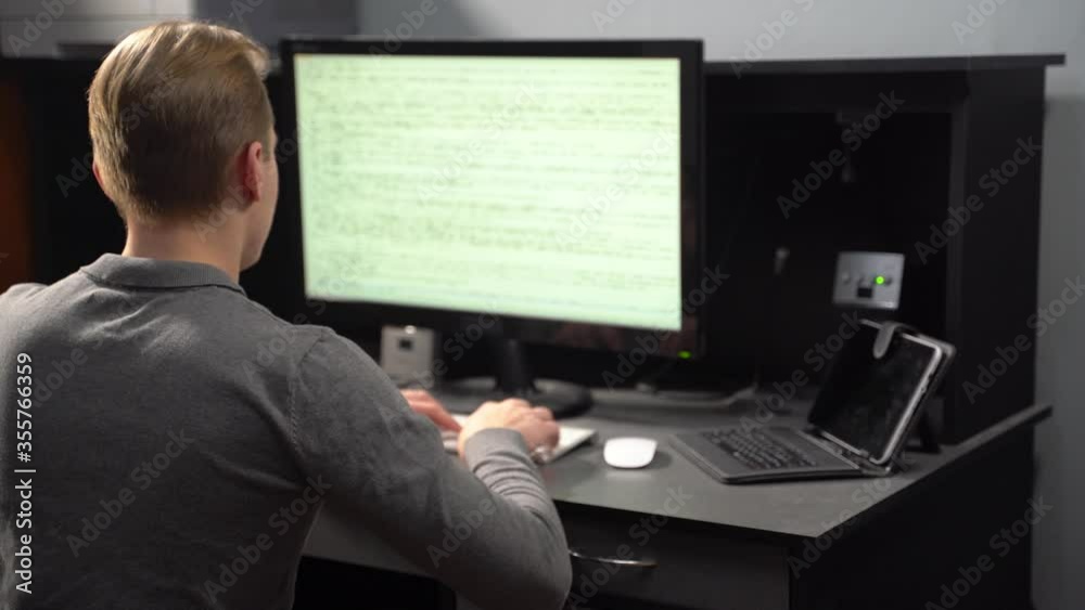 Back View of Professional IT Programer Working on Desktop Computer. Young Man working on computer in it office, sitting at desk writing codes. Programmer typing data code, working Back View of Professional IT Programer Working on Desktop Computer. Young Man working on computer in it office, sitting at desk writing codes. Programmer typing data code, working