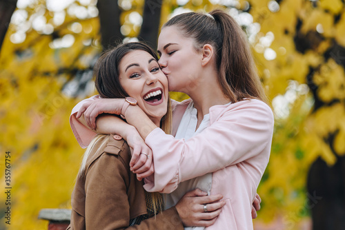 two female friends hugging happy outside with one kissing the other on her cheek