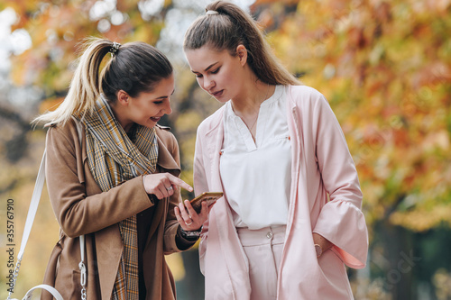 two women talking in a park, one showing the other something on her phone