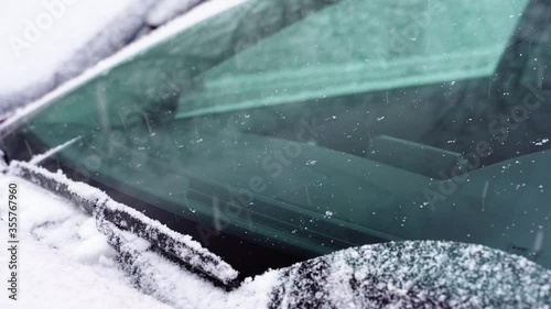 Auto Car wipers sweep snow in winter at fast speed. Automobile windshield in winter day, car wipers clean glass, snowstorm outdoors. Snowy weather. Snow covered car, closeup front view