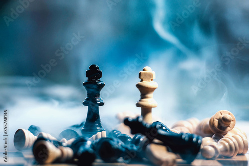 two chess figure kings of different colors standing  in smoke while all the other figures are down