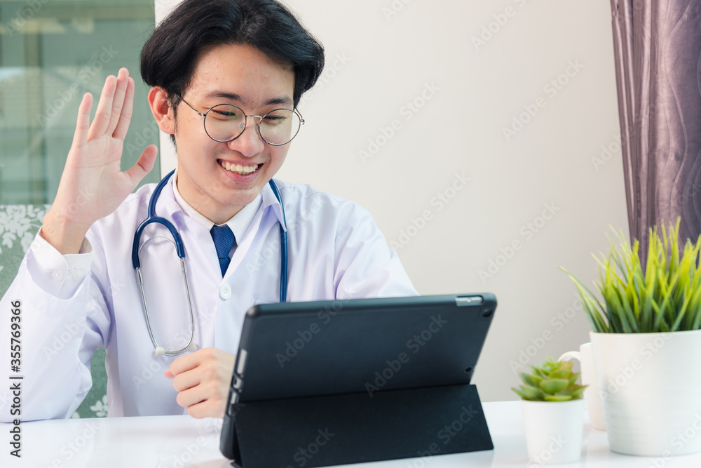 Happy Asian young doctor handsome man smile in uniform wear glasses raise hands to greet patients modern smart digital tablet computer on desk at hospital office, Technology Healthcare And Medicine Happy Asian young doctor handsome man smile in uniform wear glasses raise hands to greet patients modern smart digital tablet computer on desk at hospital office, Technology Healthcare And Medicine