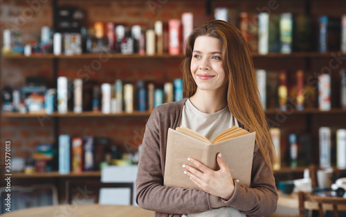 Young attractive girl reading interesting book in cafe