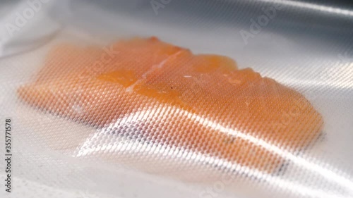 Vacuum packing machine sealing a raw salmon fish fillet in the kitchen.