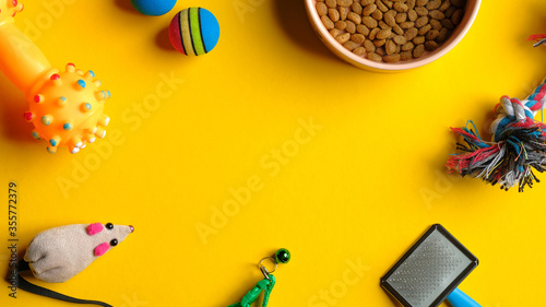 Pet care and training concept. Top view bowl of dry food and accessories for cat and dog on yellow background.