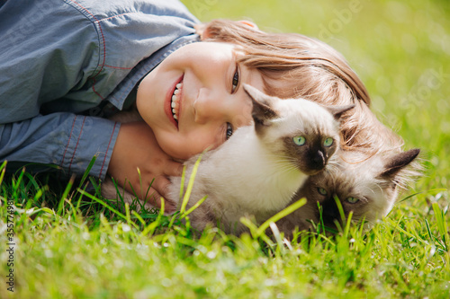 Kid plays in the summer outdoors. Сhild is friends with pet in summertime. Cute toddler is playing with a kitten on grass. Boy and baby cat photo