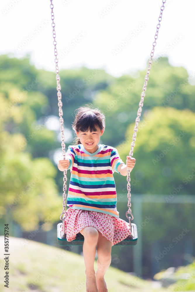 夏の公園でブランコを遊んでいる可愛い子供