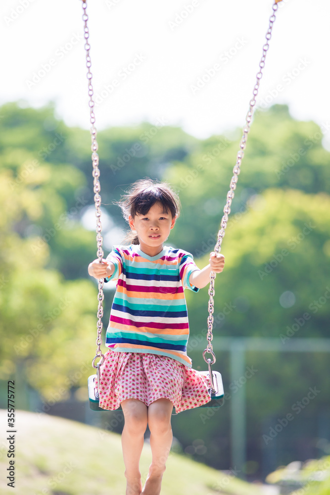 夏の公園でブランコを遊んでいる可愛い子供