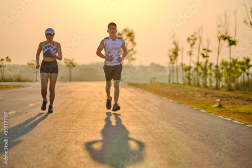 Young women and man runners run on the road during sun rise