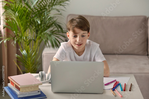 A focused boy sits on the couch and does homework at the table.