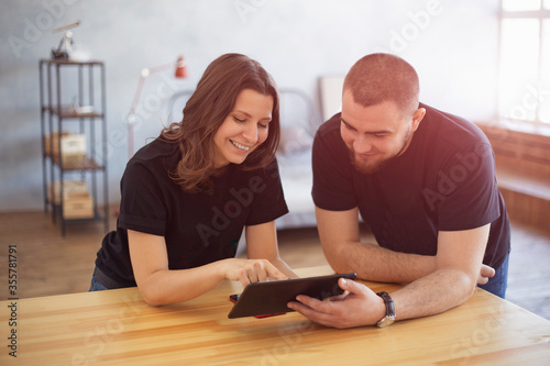 Portrait of happy young couple using a digital tablet together at home. Young man and woman looking at touch screen computer and smiling. Freelance