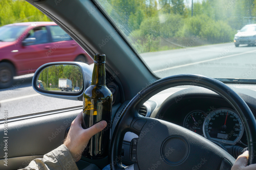 A bottle of wine in the hand of a driver traveling at high speed. Concept of unacceptable and dangerous car driving.