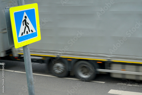   Sign of the transition on the background of a passing large truck. Road crossing danger concept at unregulated pedestrian crossing.