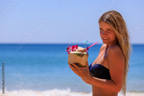 Beautiful girl in a swimsuit with coconut on the beach.