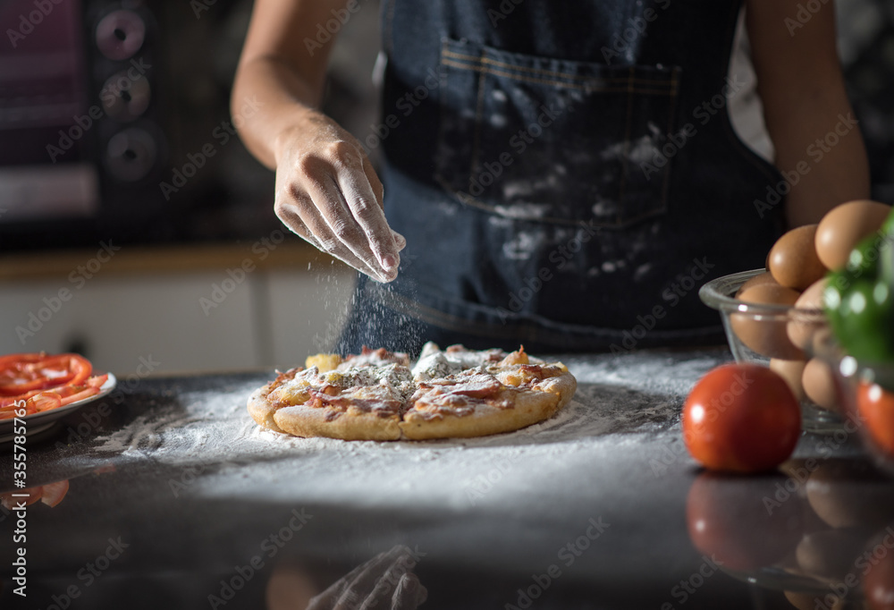 close-up of human hands in the apron knead the dough on a black wooden table, sprinkle with flour.Making dough by hands at bakery.