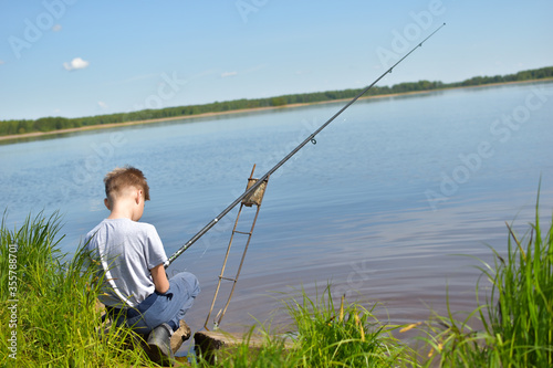 boy child fisherman sits on shore and looks at float. Fishing with children