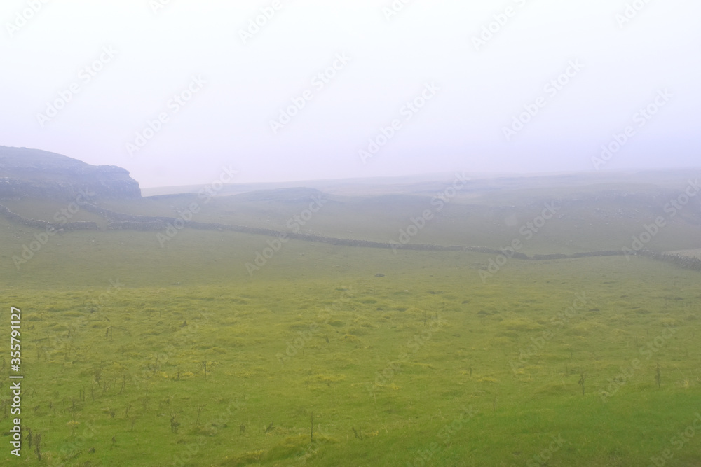 Fototapeta premium White fog cover over dandscape green grasses in flied of yorkshire dale, Malham