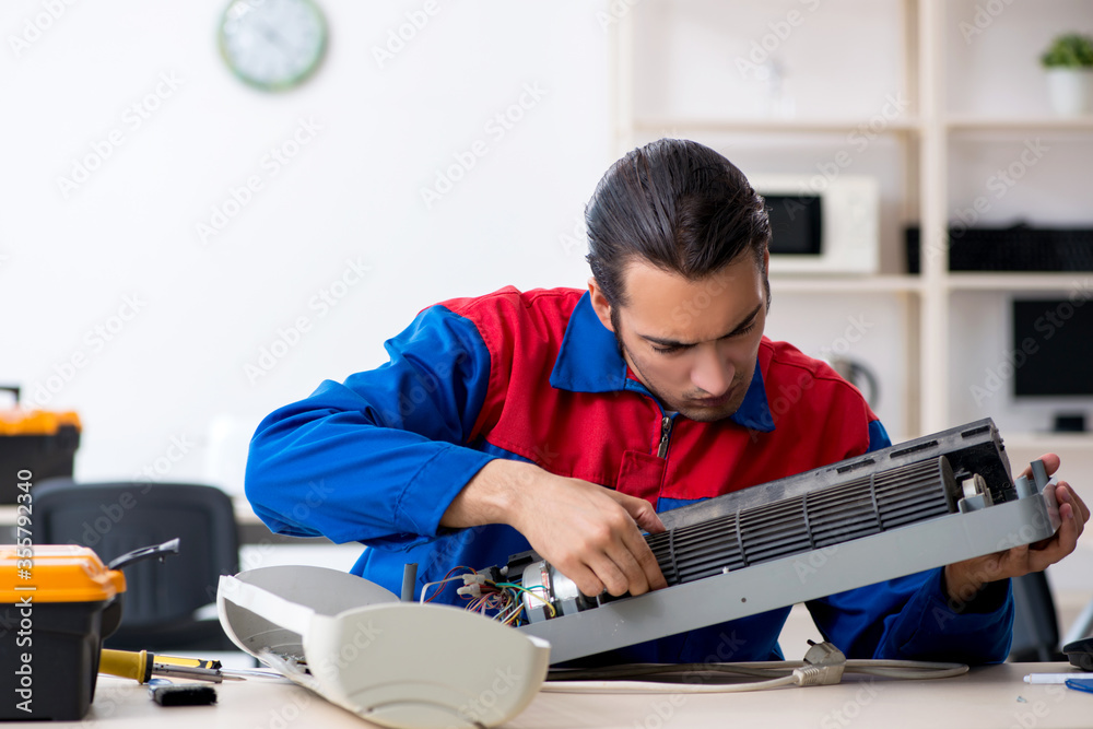Young repairman repairing air-conditioner at warranty center Young repairman repairing air-conditioner at warranty center