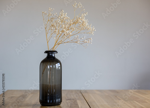 Fotografía A dark glass vase with a dry flower stands on a wooden surface.