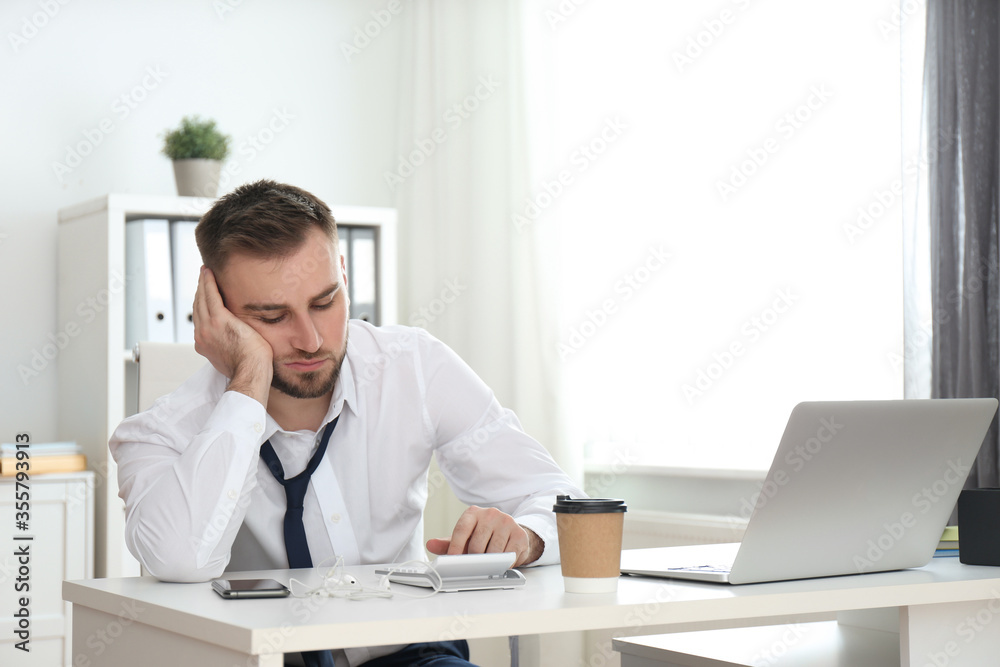 Lazy young man with calculator at table in office Lazy young man with calculator at table in office