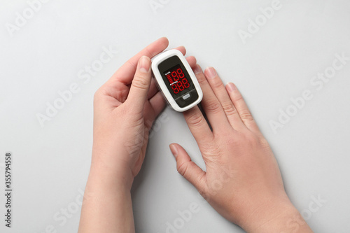 Woman using fingertip pulse oximeter on white background, top view photo