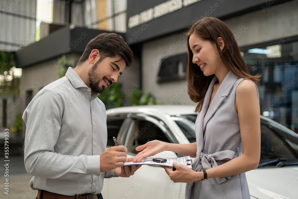 Obraz premium Auto business, car sale, consumerism and people concept - woman Sign Contract with car dealer in auto show. car salesman is making deal with lender. Used cars cheaper than new cars. But to buy a used 