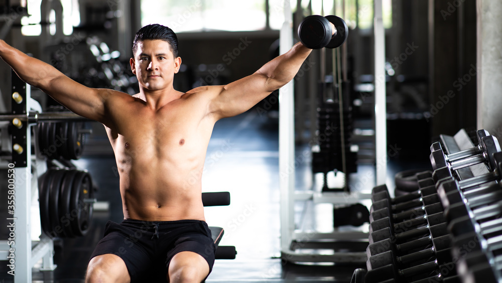 Young Man Naked bodybuilder exercising lifting with dumbbell at gym. .Gym equipment and sport concept. Fitness Healthy lifestye and workout at gym concept.