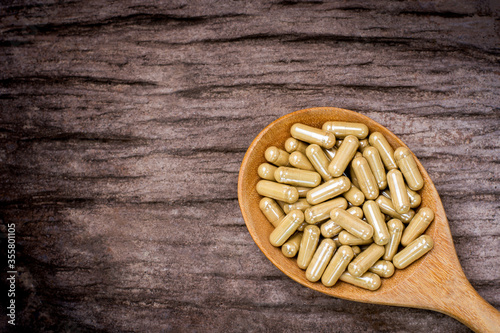 Green herbal medicine capsules in wooden spoon isolated on old rustic wood table background. Top view. Flat lay. Dark tone. Vintage style. photo