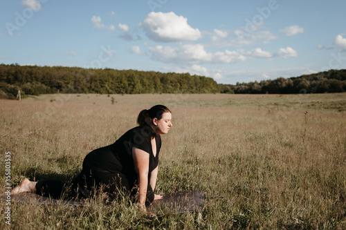 Outdoor yoga. Young overweight woman doing yoga exercise in the meadow. Open air workout, healthy lifestyle, weight loss © Vadym