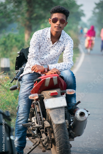 outdoor portrait of a young guy wearing sunglasses and white shirt sitting on a motor bike seat and looking at the camera