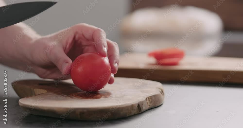 Slow motion man slicing fresh red tomato on olive board side view Slow motion man slicing fresh red tomato on olive board side view