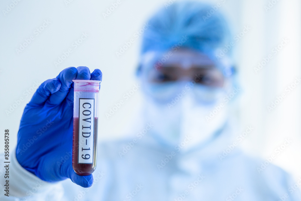Focus on Blood test tube of COVID19, Coronavirus or Novel corona virus epidemic disease. Lab technician scientist in PPE Personal Protective Equipment holding blood tube test in hospital laboratory. Focus on Blood test tube of COVID19, Coronavirus or Novel corona virus epidemic disease. Lab technician scientist in PPE Personal Protective Equipment holding blood tube test in hospital laboratory.