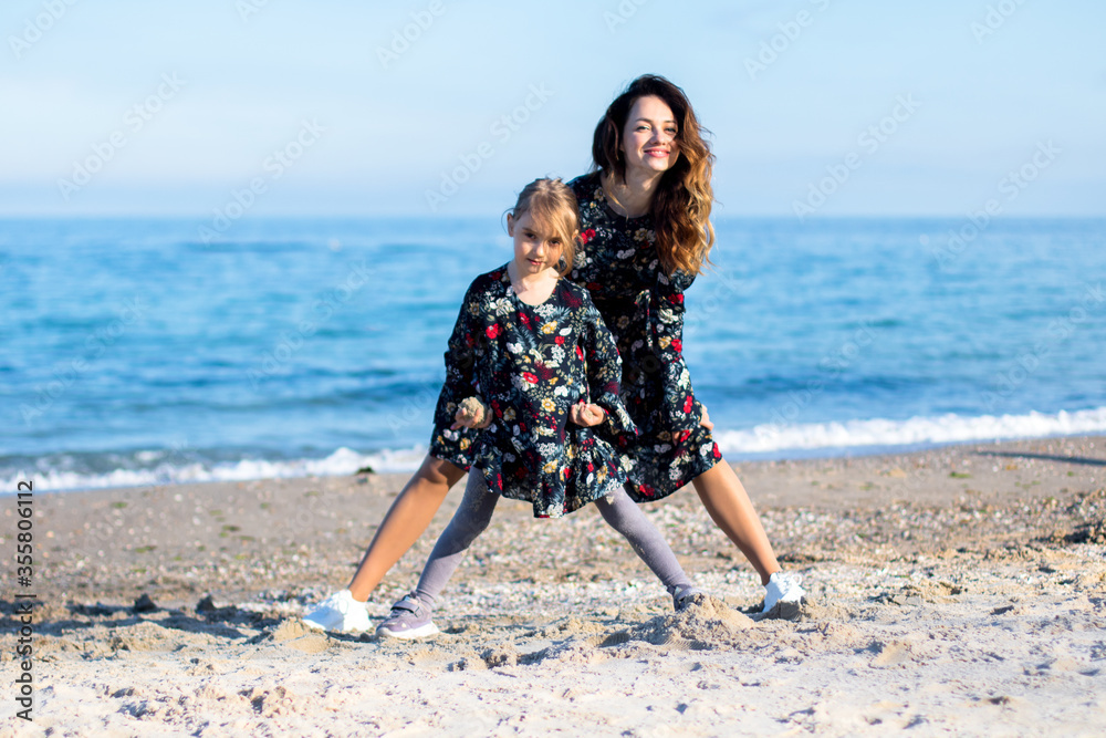 young woman and little girl in similar dresses are playing on the beach young woman and little girl in similar dresses are playing on the beach