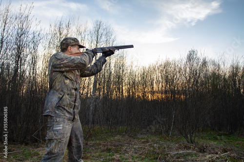 a hunter takes aim with a shotgun at dusk in a spring forest
